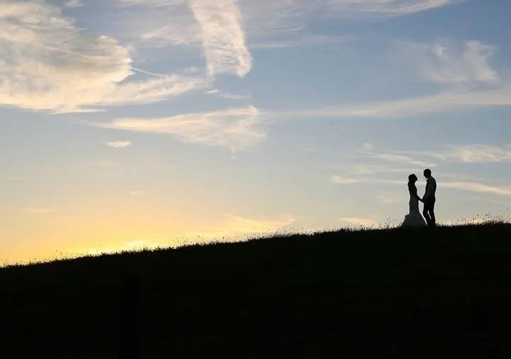 Silhouette of a bride and groom holding hands on a hilltop at sunset